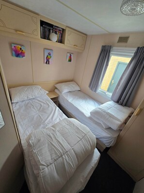 Ein Schlafzimmer mit zwei Betten, einem Bücherregal und einem Fenster mit Vorhängen.