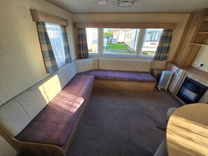 A compact RV interior with a seating area, a small kitchenette, and a view of the outside. - Towyn Oakfields  F70 (Kinmel Bay)