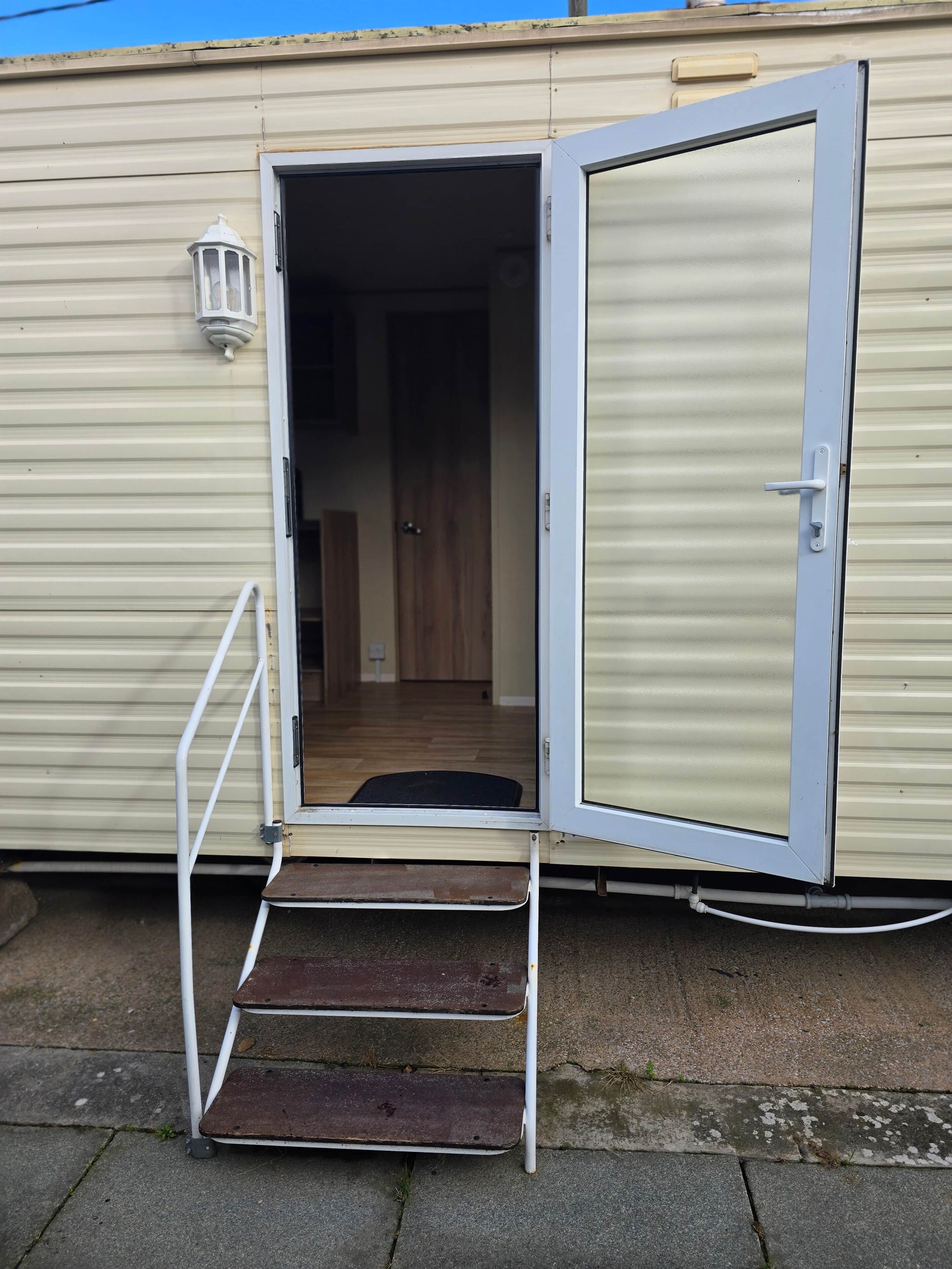 A mobile home with an open door, a small set of steps leading inside, and a visible interior hallway.