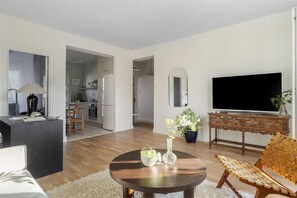 A modern living room with a sofa, a coffee table, a TV, and a kitchen in the background.