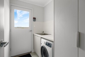 Uma lavanderia compacta com máquina de lavar, uma pia pequena e uma porta com janela.