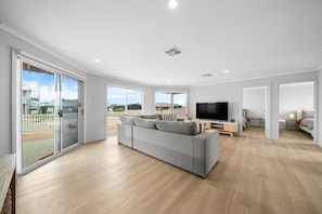 A spacious living area with a grey sofa, a flat-screen TV, and a sliding glass door leading to a balcony.