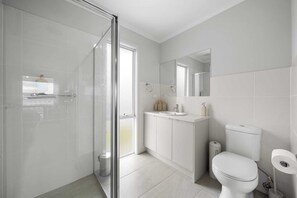 Uma casa de banho moderna com cabine de duche em vidro, lavatório branco e sanita.