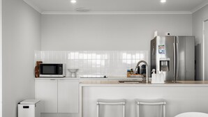 Una cocina moderna con armarios blancos, un refrigerador de acero inoxidable, un microondas y un lavamanos.