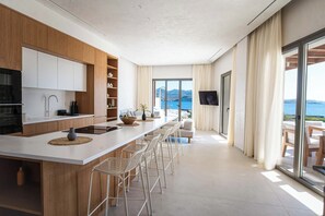 Eine moderne Küche mit einer langen Kochinsel, Barhocker und Blick aufs Meer.