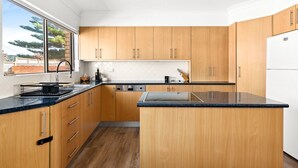 A modern kitchen with wooden cabinets, a black countertop, and a built-in dishwasher. - Oceanview 3-Bedroom Apartment in Kiama (Kiama)