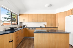 A modern kitchen with wooden cabinets, a black countertop, and a built-in dishwasher. - Oceanview 3-Bedroom Apartment in Kiama (Kiama)