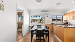 A modern kitchen with a dining area, wooden cabinets, and a large window. - Oceanview 3-Bedroom Apartment in Kiama (Kiama)