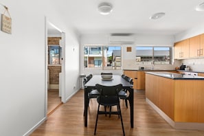 A modern kitchen with a dining area, wooden cabinets, and a large window. - Oceanview 3-Bedroom Apartment in Kiama (Kiama)
