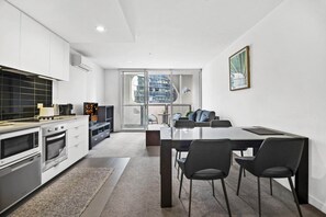 Eine moderne Küche mit weißen Schränken, einem Essbereich mit einem Glastisch und Blick auf die Stadt durch große Fenster.