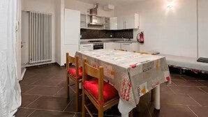 Uma área de refeições com mesa, cadeiras, um radiador e uma cozinha ao fundo.