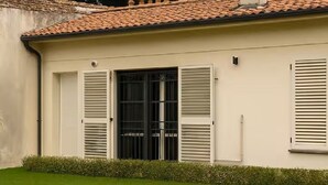 Um edifício com telhado em telhas, uma grande porta central com persianas e uma pequena janela à direita.