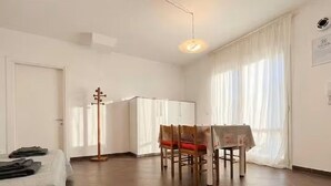 Um quarto com uma cama, uma mesa de jantar com cadeiras, um cabideiro e uma janela com cortinas.