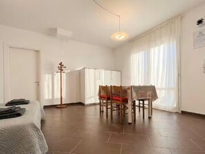Habitació amb un llit, una taula de dinar amb cadires, una perxa i una finestra amb cortines.