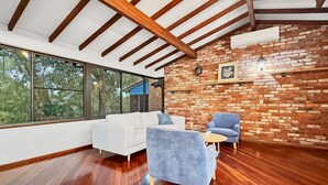 Un intérieur moderne avec un canapé blanc, un fauteuil bleu et une petite table. On peut voir un mur en briques et des poutres en bois.