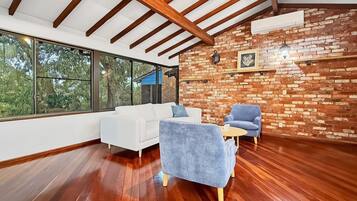 A modern interior with a white sofa, blue armchair, and a small table. A brick wall and wooden beams are visible.