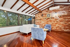 A modern interior with a white sofa, blue armchair, and a small table. A brick wall and wooden beams are visible.