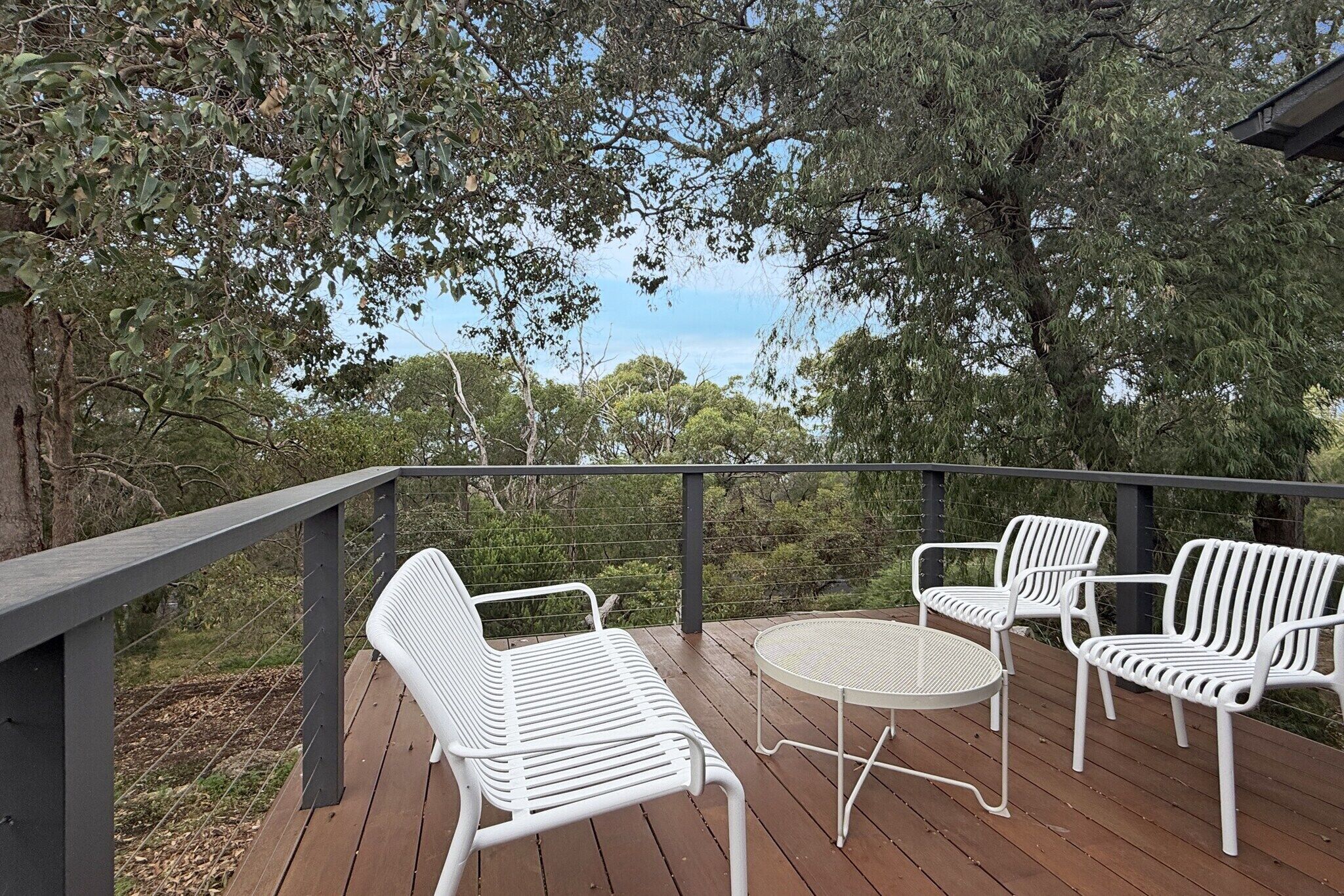 Une terrasse en bois avec des chaises et une table en métal blanc, donnant sur un paysage naturel.