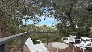 Une terrasse en bois avec des chaises et une table en métal blanc, donnant sur un paysage naturel.