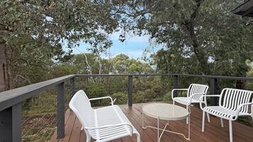 Une terrasse en bois avec des chaises et une table en métal blanc, donnant sur un paysage naturel.