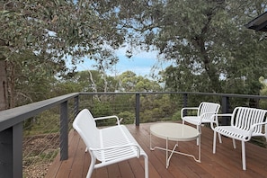 A wooden deck with white metal chairs and a table, overlooking a natural landscape.