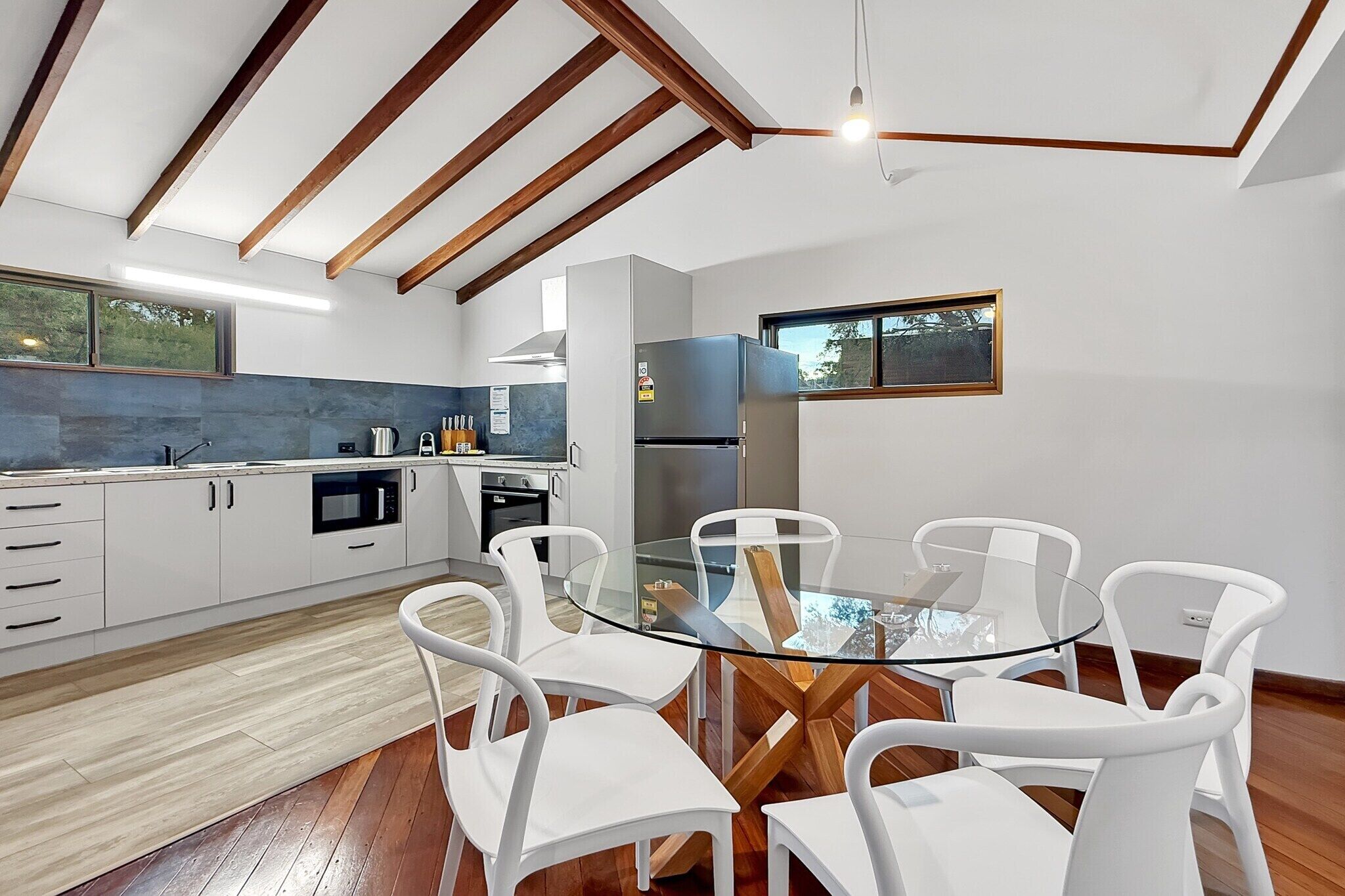 A modern kitchen with white cabinetry, a glass dining table, and white chairs.
