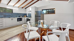 Une cuisine moderne avec des meubles blancs, une table à manger en verre et des chaises blanches.