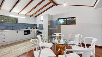 A modern kitchen with white cabinetry, a glass dining table, and white chairs.