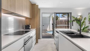 Une cuisine moderne dotée d’appareils électroménagers en acier inoxydable, de meubles en bois et offrant une vue sur un jardin avec une piscine.