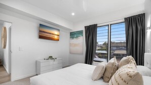 Une chambre à coucher moderne avec un grand lit, une table de chevet, une commode et une fenêtre avec des rideaux.