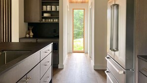 A modern kitchen with a built-in refrigerator, wooden ceiling, and a view through a door to an outdoor area.