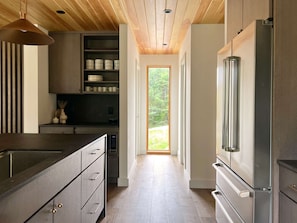Eine moderne Küche mit Einbaukühlschrank, Holzboden und Blick durch eine Tür in einen Außenbereich.