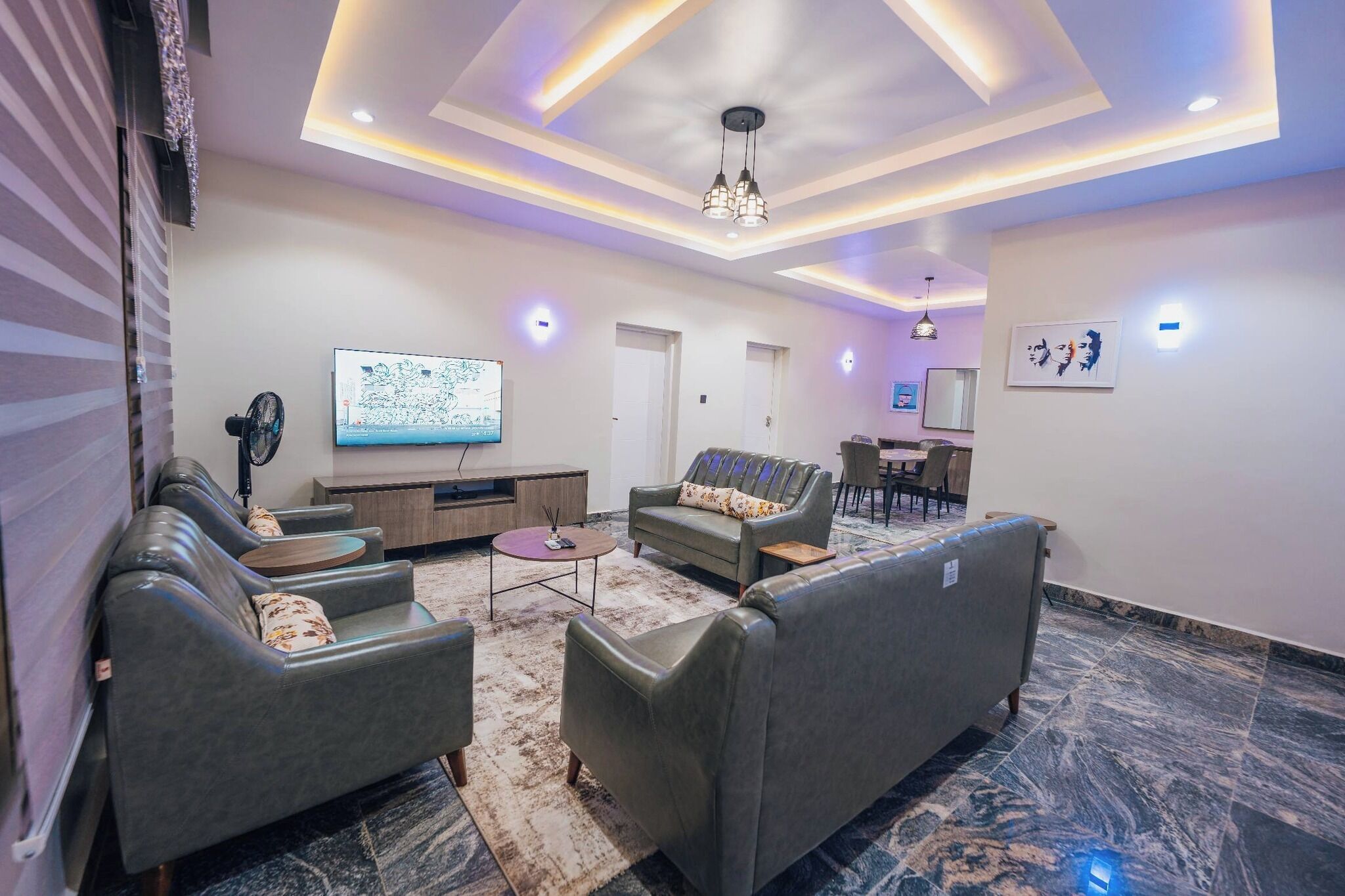 A modern living room with leather sofas, a flat-screen TV, and a dining area with chairs.