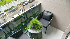 Een balkon met twee stoelen, een tafeltje met een plant en uitzicht op de straat.