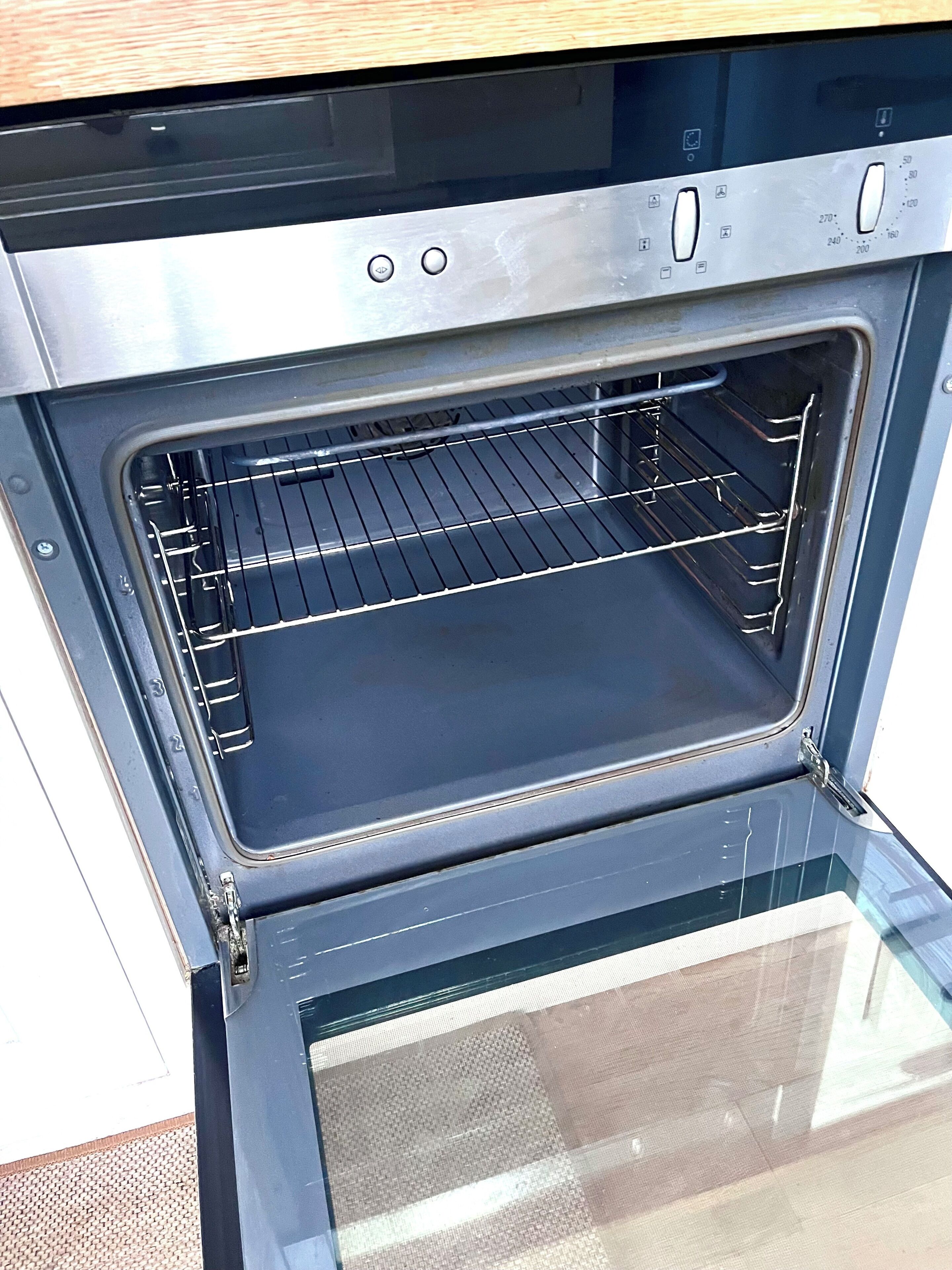An open oven with a metal rack inside, a control panel with temperature settings, and a glass door.