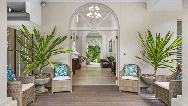 A hallway with wicker furniture, potted plants, and a view into a room with a large window. - Spacious 7-Bed Family Home in Chapel Hill (Chapel Hill)