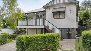 A two-story house with a balcony, a covered porch, and a fenced yard. - Relaxing Stay Near Brisbane’s Cultural Heart (Norman Park)