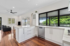 Cocina moderna con muebles blancos, lavavajillas integrado y un amplio ventanal con vistas a zonas verdes.