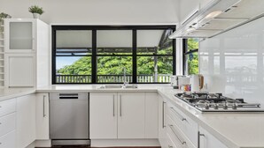 A modern kitchen with white cabinets, a dishwasher, a stove, and a large window with a view of greenery. - Relaxing Stay Near Brisbane’s Cultural Heart (Norman Park)