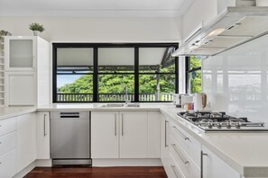 Eine moderne Küche mit weißen Schränken, einem Geschirrspüler, einem Herd und einem großen Fenster mit Blick auf Grünflächen.