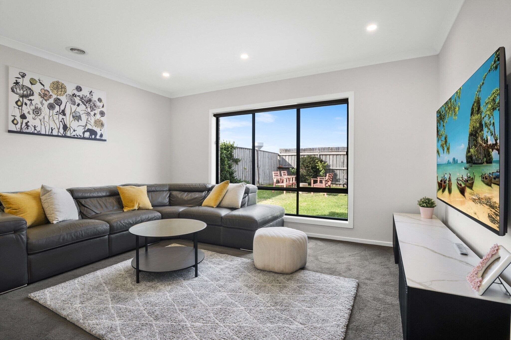 A modern living room with a sectional sofa, a round coffee table, and a large window offering a view of the backyard.