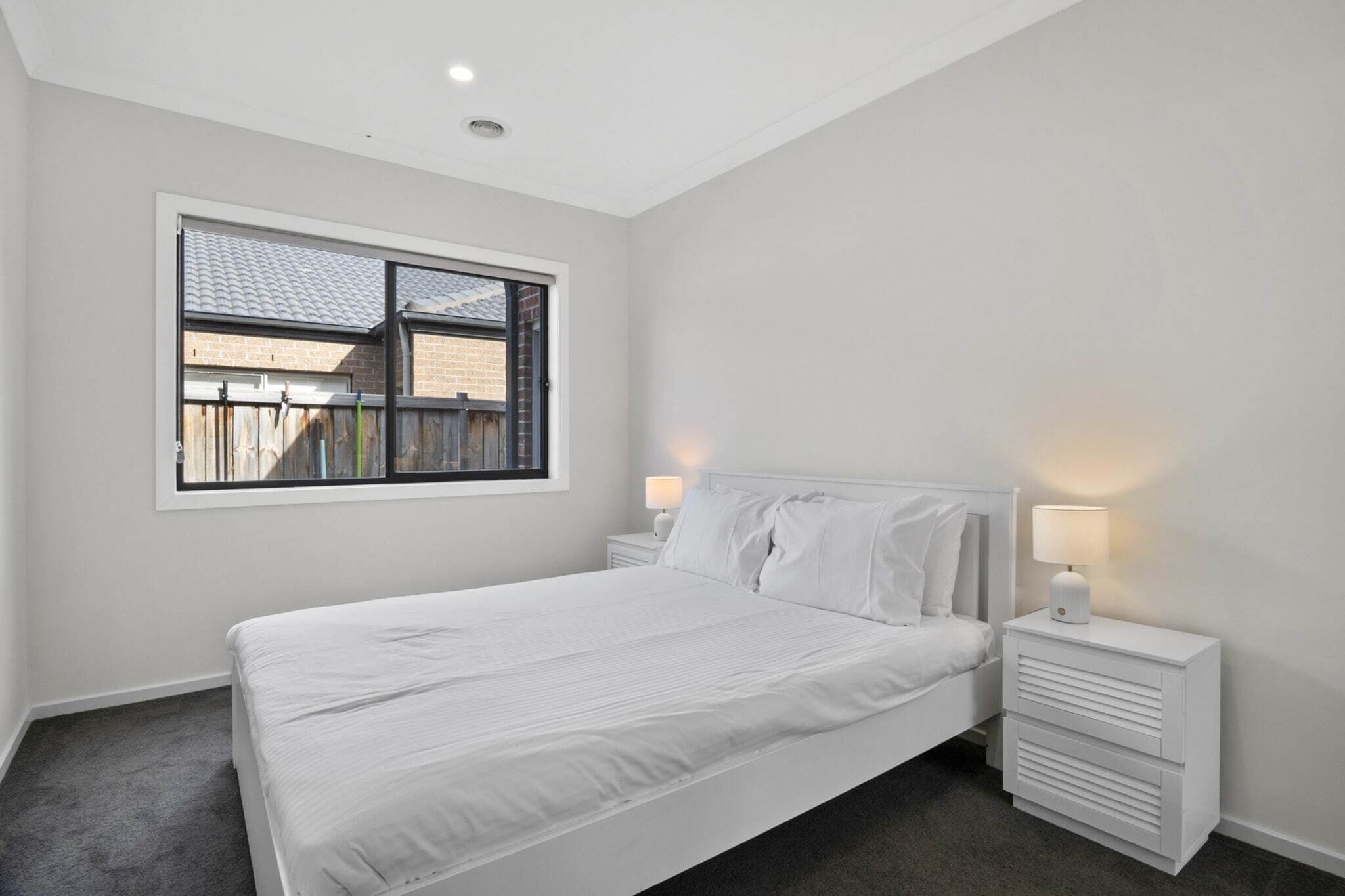 A bedroom with a bed, a nightstand, a window, and a view of a brick building.
