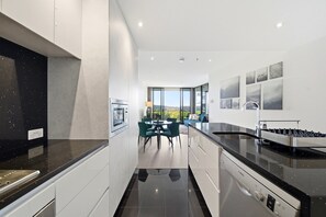 A modern kitchen with a black countertop, white cabinetry, and a dining area with green chairs. - Stylish 1BR CBD w/ Parking Lot (City)