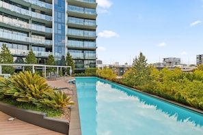 A modern building with a swimming pool, surrounded by greenery and a clear sky. - Stylish 1BR CBD w/ Parking Lot (City)
