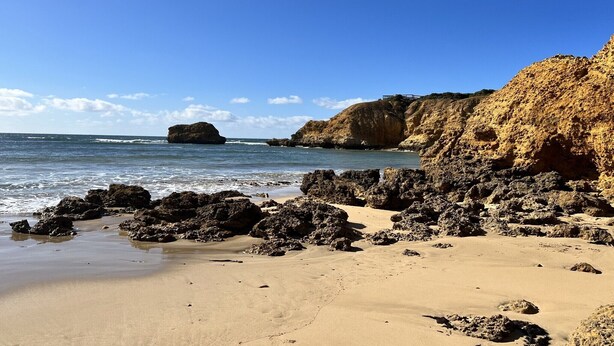 Une plage avec des formations rocheuses et un ciel bleu dégagé.