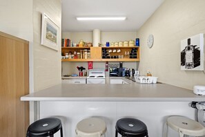 A kitchen with a central island, bar stools, a stove, and various kitchen items on shelves. - Airy & Arty 2-Bed Old Kingston Foreshore (Kingston)