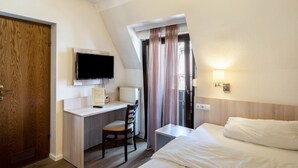 Ett hotellrum med ett skrivbord, en stol, en säng, en TV och ett fönster med gardiner.
