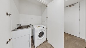 Un lavadero con lavadora, un lavabo y una puerta que da a otra habitación.