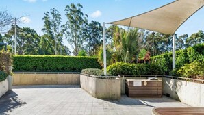 Un espacio al aire libre empedrado con macetas, un banco de madera y una estructura grande que da sombra.