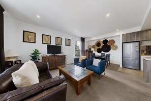 Ein modernes Wohnzimmer mit einer Ledersofa, blauen Sessel, einem Couchtisch, einem Flachbildfernseher und einer Wanddekoration.